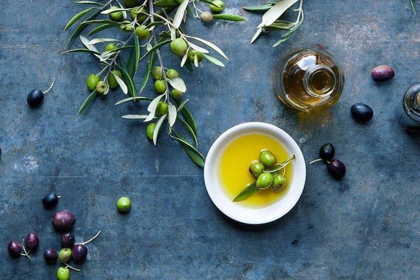 A bowl of olive oil with olives and branches on a textured surface. 2