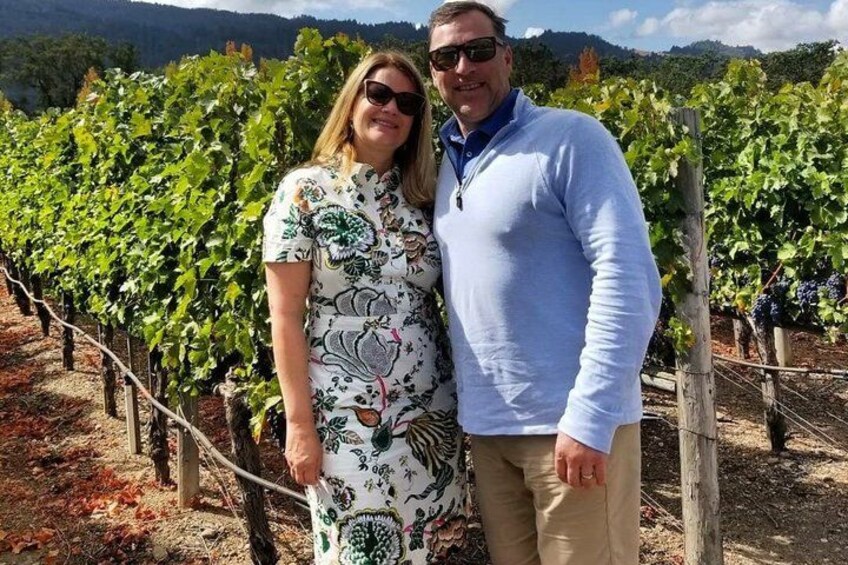 Two people standing in a vineyard with rows of grapevines. 5