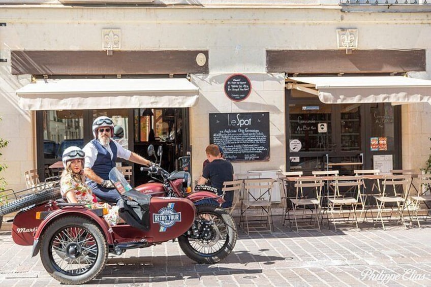 A vintage motorcycle with a sidecar, a café with outdoor seating, and a signboard with text. 2