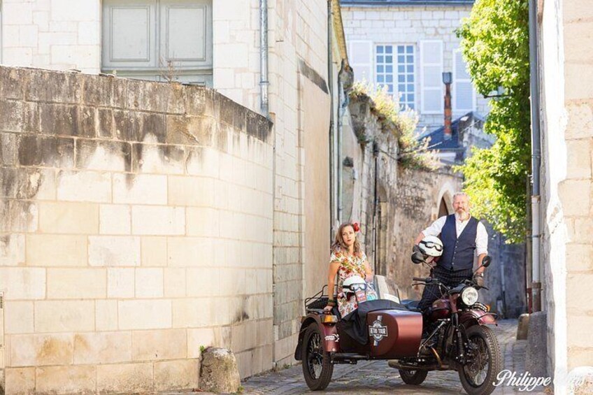 A narrow street with a vintage motorcycle and a sidecar, a stone wall, and a building with a window. 3