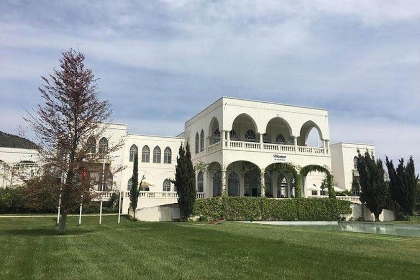 A white building with arched windows and a balcony, surrounded by a well-maintained lawn and trees. 5