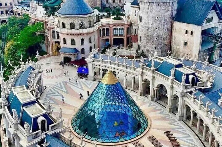 Eine große gläserne Pyramidenstruktur, umgeben von verzierten Gebäuden und einem schlossartigen Bau. 5