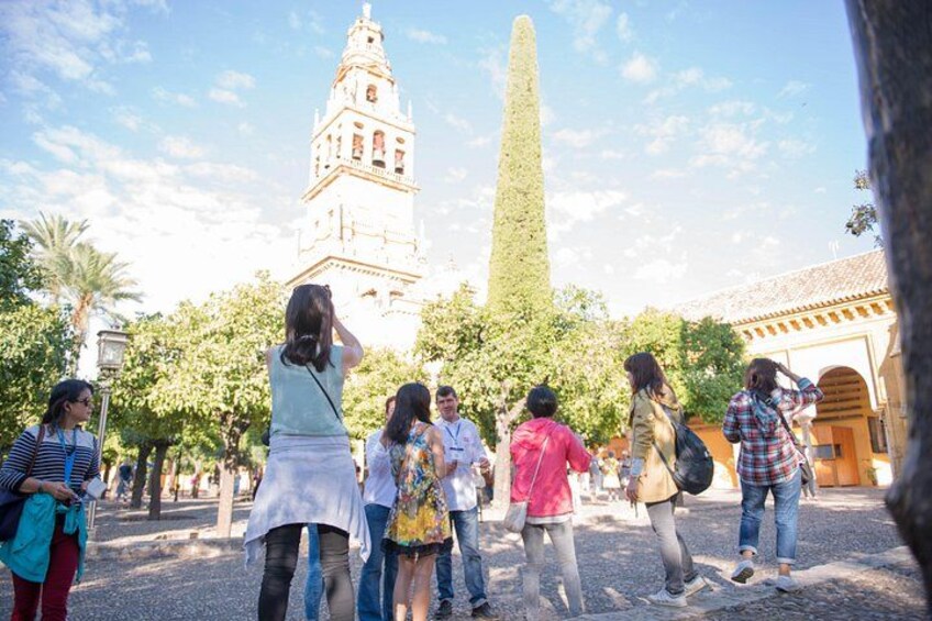 Un grupo de personas de pie en una plaza, con una torre alta y un monumento imponente al fondo. 2
