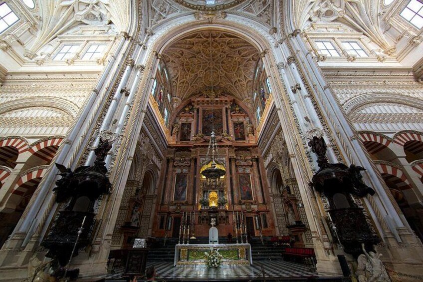 Interior de una iglesia ornamentada con techos altos, detalles tallados y un altar central. 3