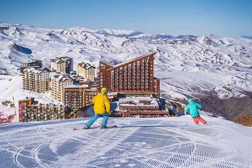 A ski slope with skiers, a ski lift, and a mountain resort in the background. 1