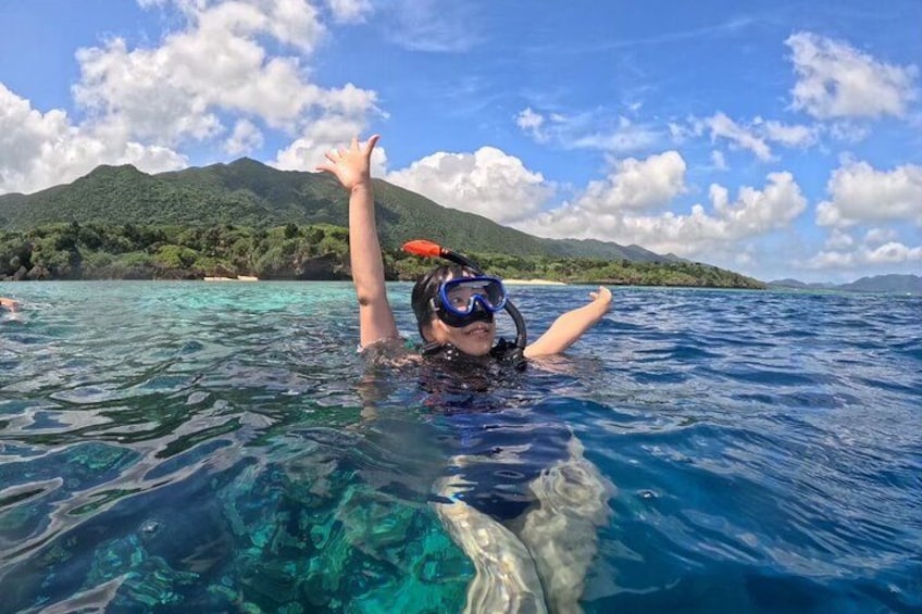 A person snorkeling in clear blue water with a mountainous landscape in the background. 3