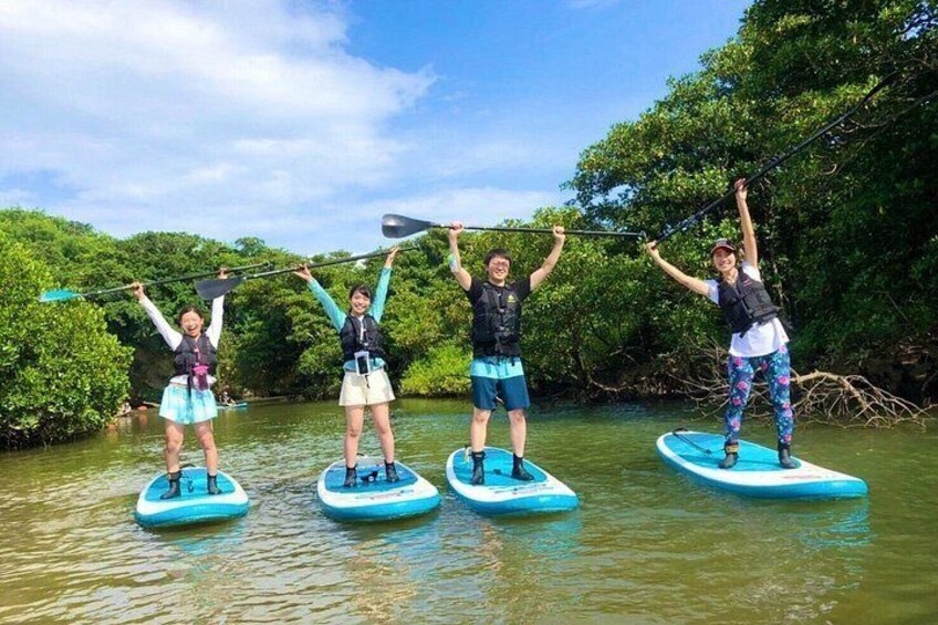 Quattro persone che fanno paddleboarding su un fiume tranquillo, circondate da vegetazione lussureggiante. 3