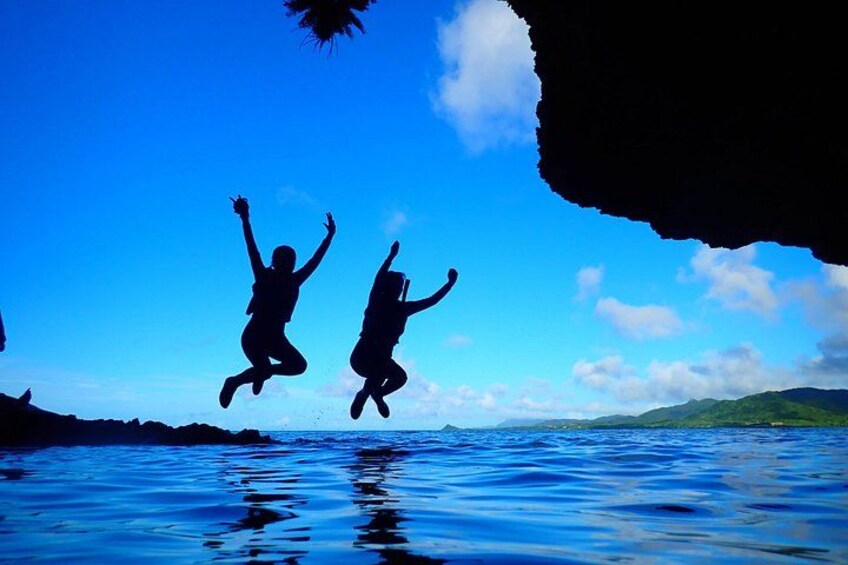 Two people jumping into water with a clear sky and distant hills. 4