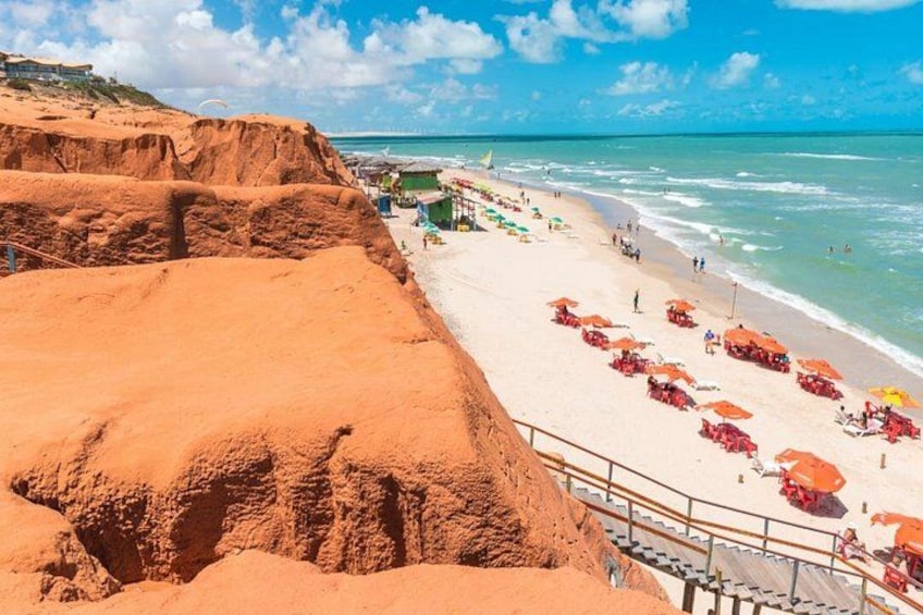 A beach with red sand, a staircase, and beach umbrellas. 3