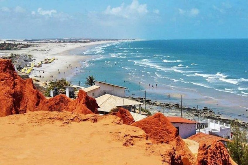 Eine Küstenlandschaft mit Strand, Ozeanwellen und rötlich gefärbten Felsformationen. 2