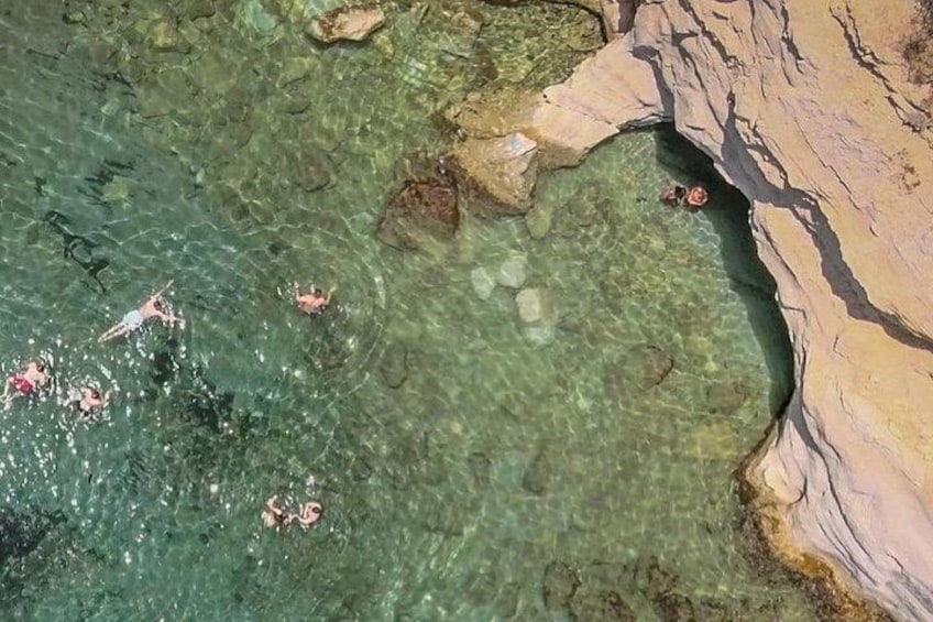 A clear blue sea with people swimming and a rocky shoreline. 3