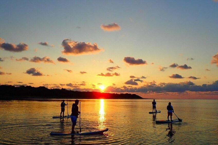 A sunset over a calm body of water with paddleboarders. 4
