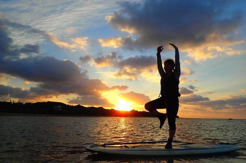 A person performing a yoga pose on a surfboard by the water during sunset. 3
