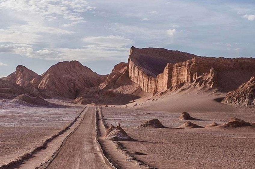 Paisaje desértico con un camino de tierra que se dirige hacia una gran formación rocosa. 3