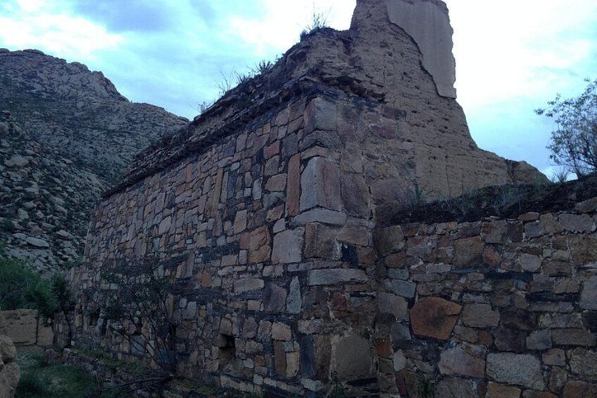 A stone building with a steep roof, surrounded by rocky terrain and sparse vegetation. 3