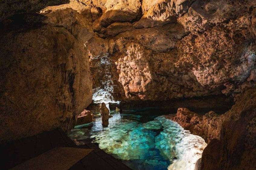 A cave interior with stalactites and a person standing in a pool of water. 3