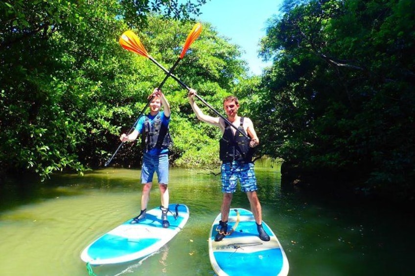 Zwei Personen stehen auf Paddleboards auf einem Fluss, umgeben von üppiger Vegetation. 4