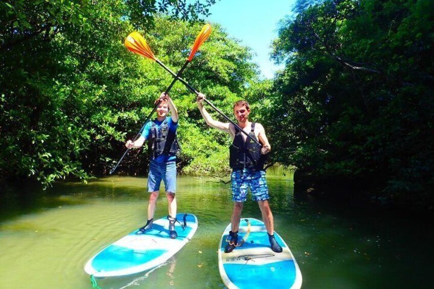 Two people paddleboarding on a calm river surrounded by dense greenery. 2