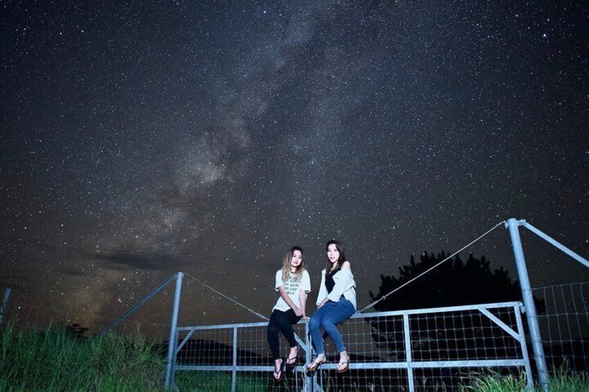 Two people sitting on a fence under a starry night sky. 1