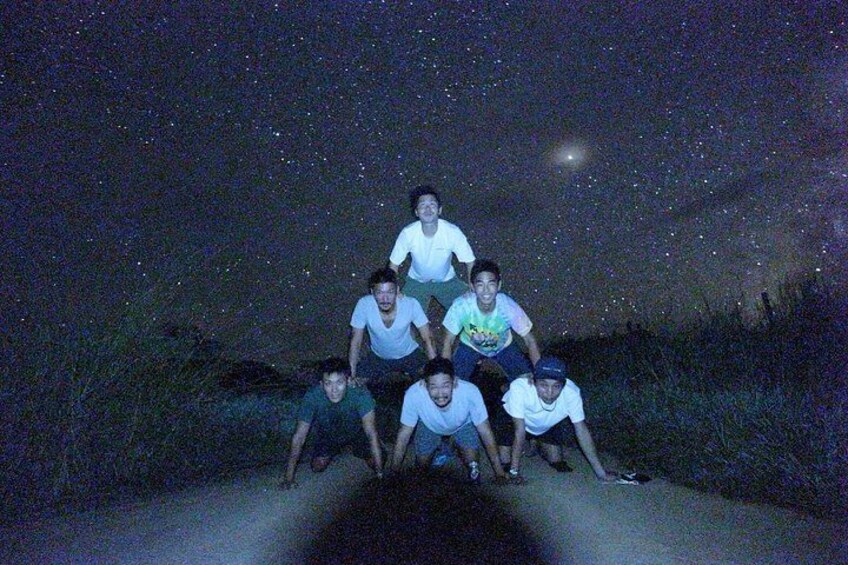 A group of people posing on a road at night under a starry sky. 5