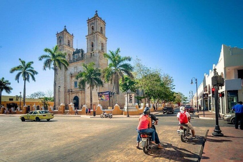 Une église historique dotée de deux tours, des palmiers, un taxi jaune et des personnes à vélo. 3