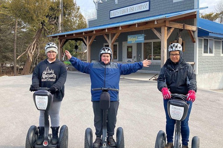 Tres personas en segways frente a un edificio con un cartel que dice 'RAILEY'S HARBOR FISH COMPANY'. 2