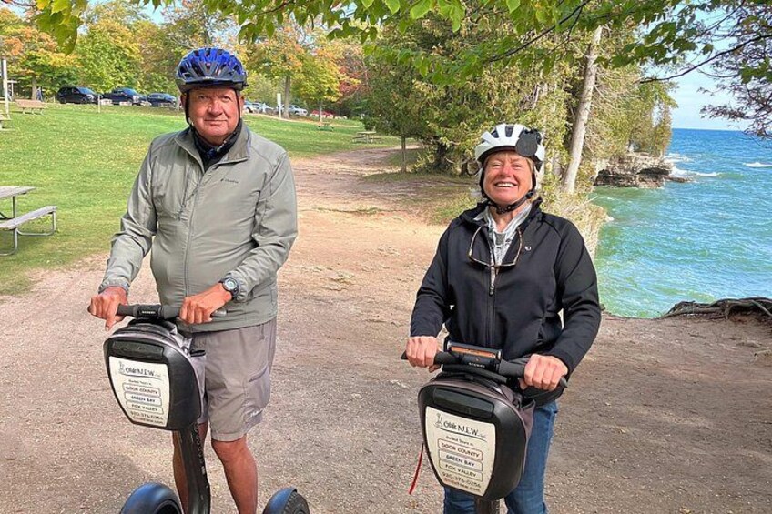 Two people on electric scooters with a body of water and trees in the background. 3