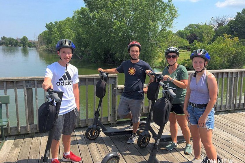 Cuatro personas en un muelle de madera junto a un lago, algunas con bicicletas y otras con scooters eléctricos. 5