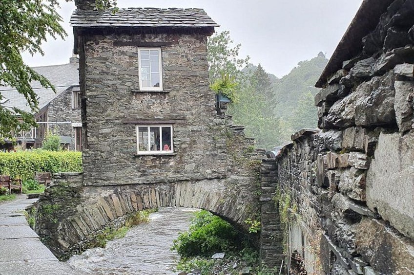 A stone building with a small archway, surrounded by greenery and other stone structures. 2