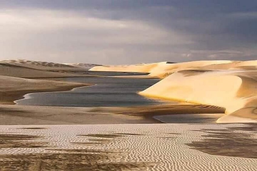 A desert landscape with sand dunes and a body of water. 3