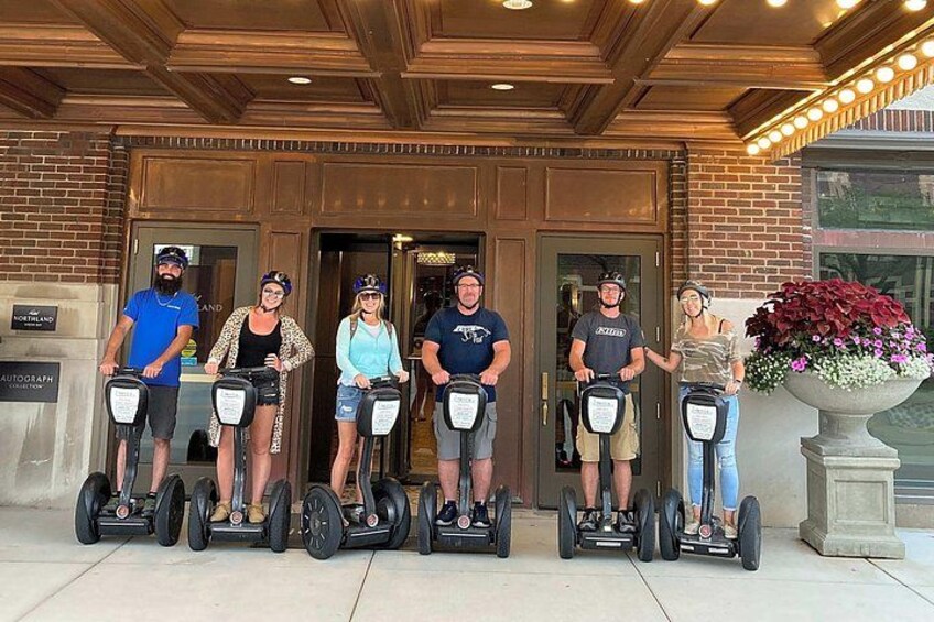 A group of people on segways in front of a building with a brick facade and a large planter with flowers. 3
