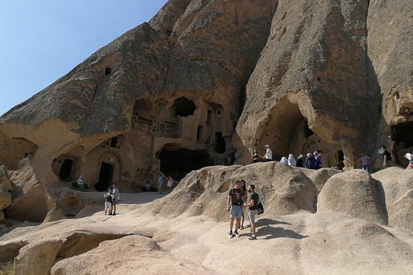 Un paysage rocheux parsemé de grottes aménagées et habité, où l’on peut voir des personnes en train d’explorer les environs. 4