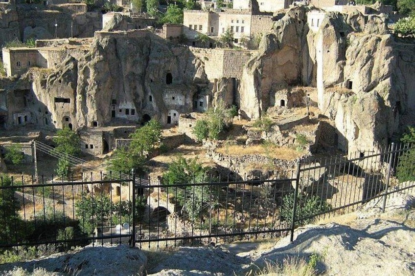 Un paysage rocheux parsemé de structures anciennes construites à même les falaises, une zone délimitée par une clôture et une végétation clairsemée. 5