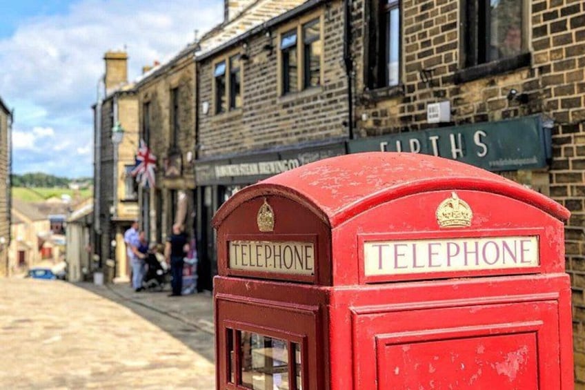 A red telephone booth in front of a brick building with a sign that reads 'FIRTHS.' 1