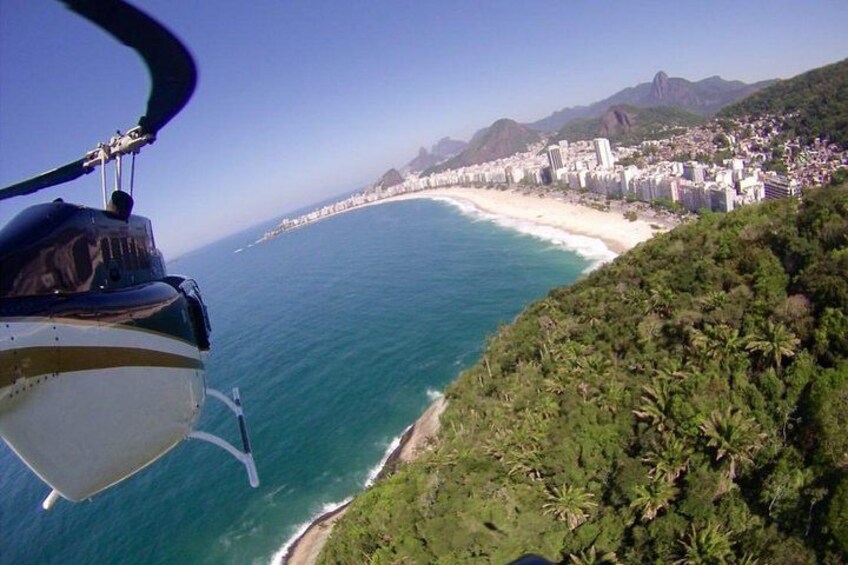 En helikopter flyger över en kuststad med en strand och berg i bakgrunden. 1