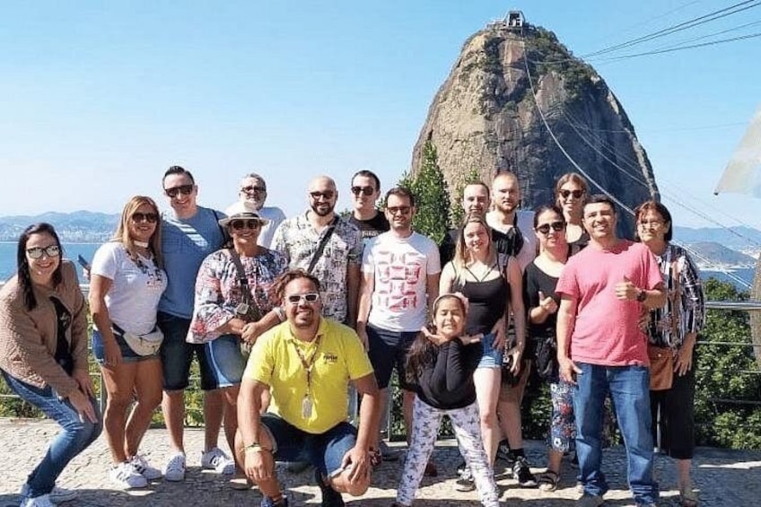 A group of people posing in front of a large rock formation with a clear sky in the background. 3