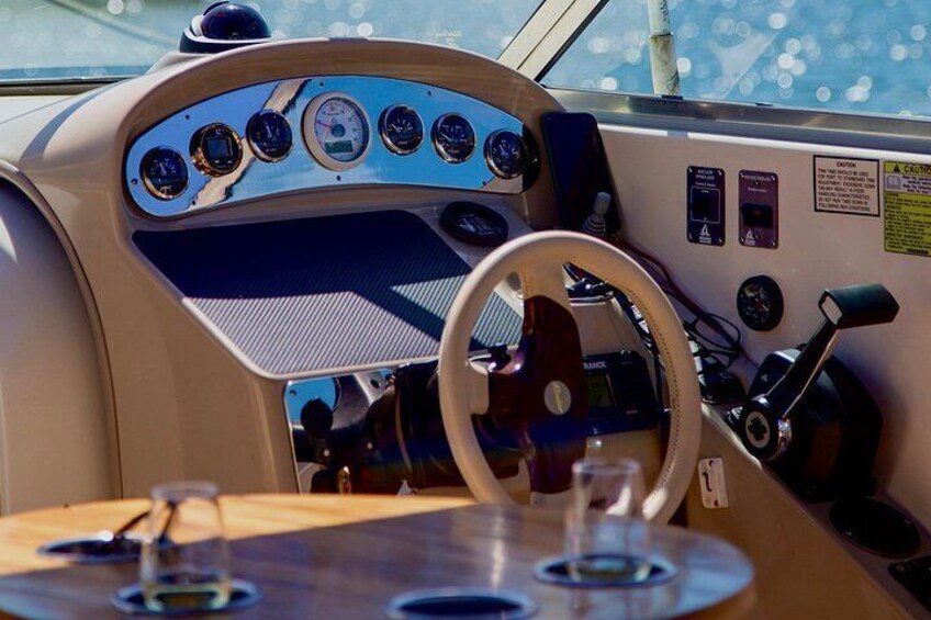 A boat's control panel with multiple gauges, a steering wheel, and a table with glasses. 5