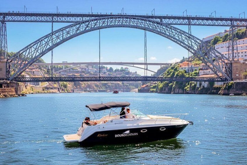 A boat named 'Douradman' on a river with a bridge in the background. 1