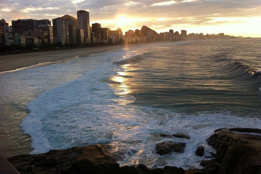 Una playa con olas, el horizonte de una ciudad y un atardecer. 2