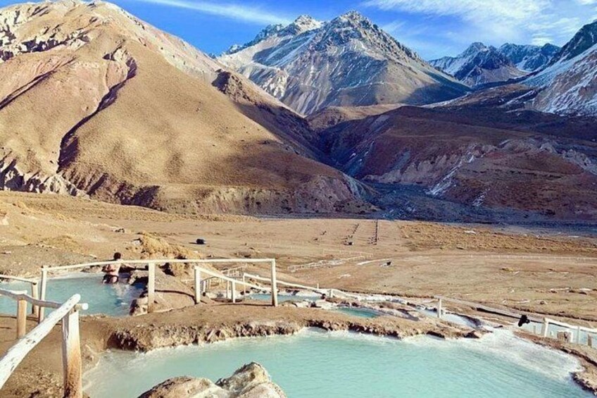 A hot spring area with wooden walkways, surrounded by mountains. 1
