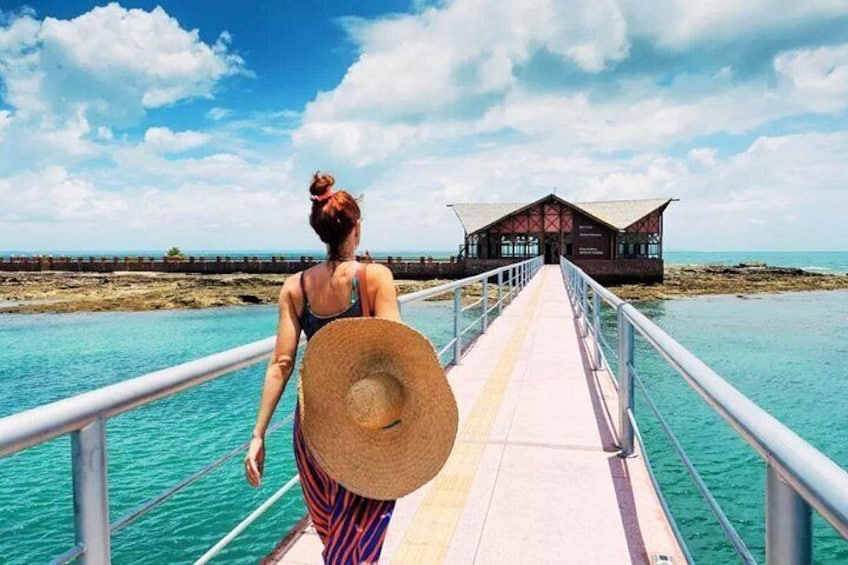 A woman walking on a pier towards a wooden structure with a thatched roof. 1