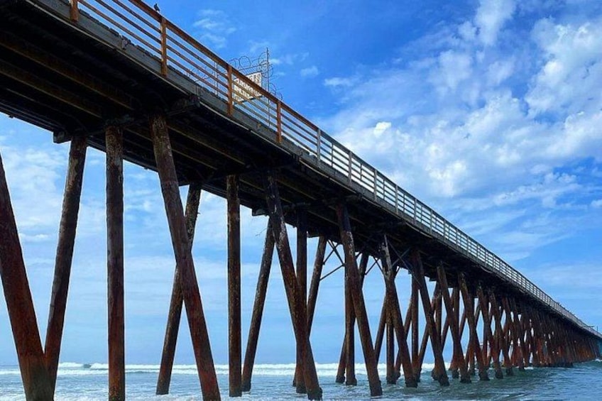 A pier with a metal railing extending over water, supported by wooden beams. 2