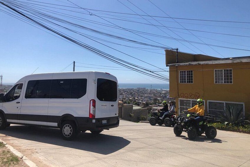 A white van parked on a street, a yellow building, and two people on a quad bike. 2