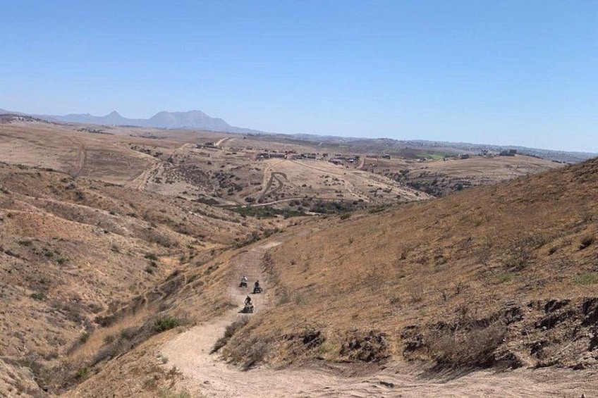 A dry, hilly landscape with a dirt path leading to a small settlement. 5