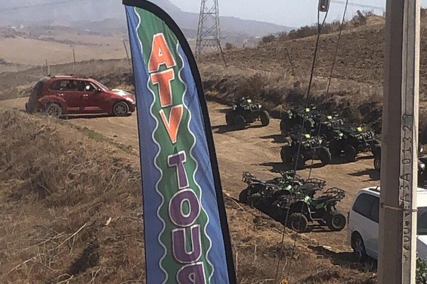 A red car, ATVs, and a white vehicle on a dirt road with a flag in the foreground. 3