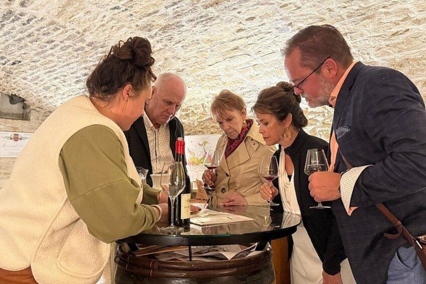 A group of people standing around a table with wine bottles and glasses. 2