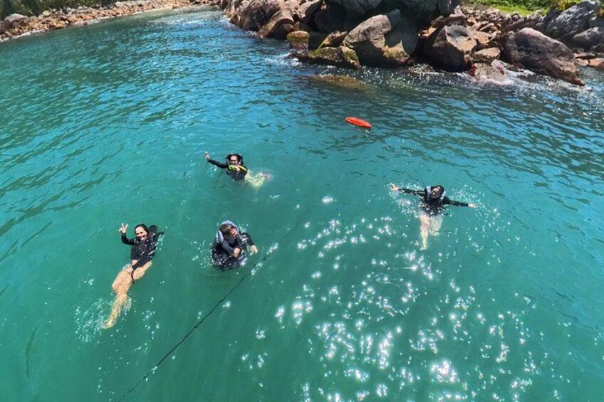 Four people swimming in clear blue water with rocks in the background. 4