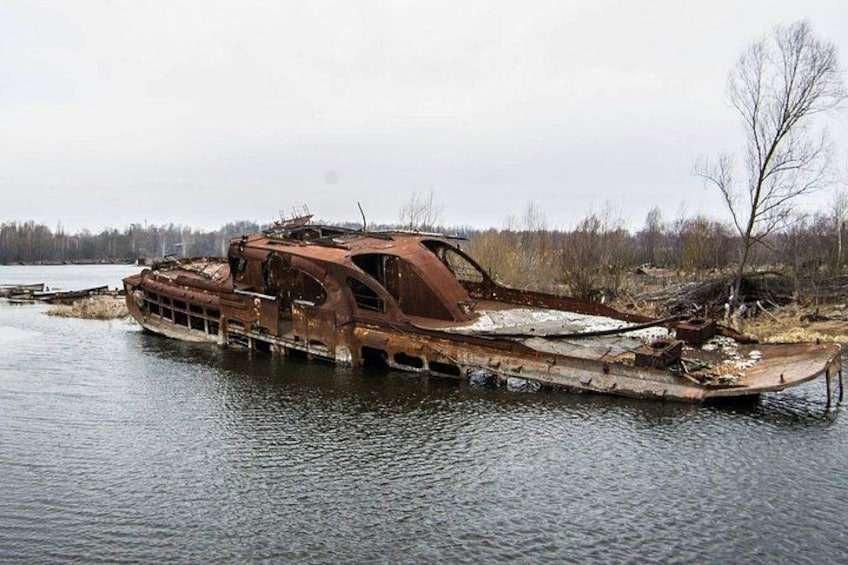 A rusted, abandoned boat in a body of water with overgrown vegetation and a barren landscape in the background. 2