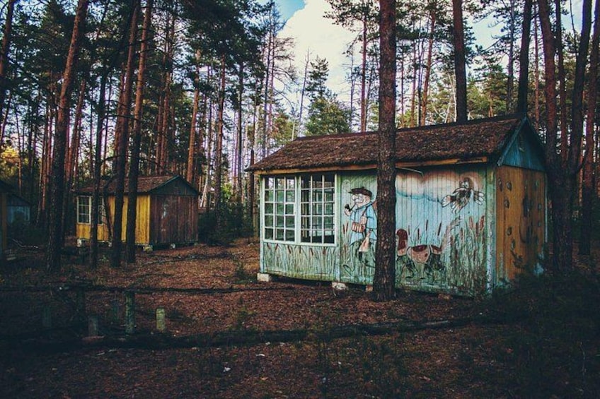 A forest with several small wooden cabins, one with colorful graffiti. 4
