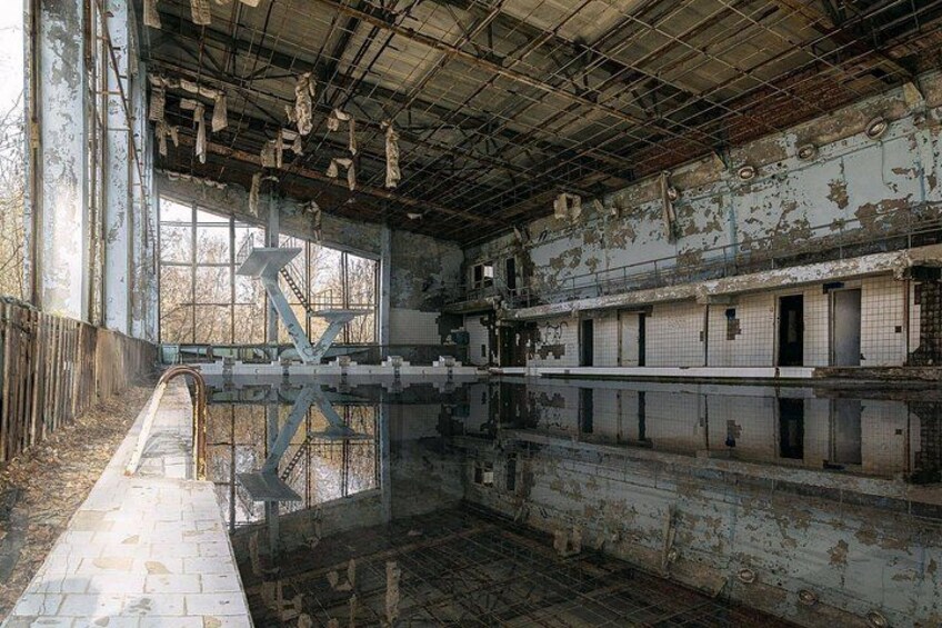 An abandoned building with a large pool, peeling paint, and rusted metal structures. 5